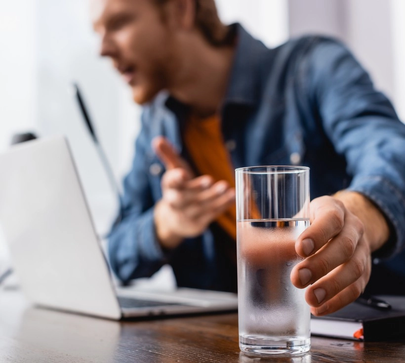 homem no computador segurando copo de água cheio